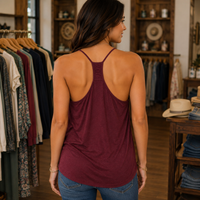 A woman viewed from behind wearing a sleeveless open-back tank top in burgundy, standing inside a boutique with clothing racks and wooden shelving visible.