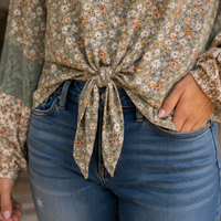 A close-up of a person wearing a beige floral long-sleeve top tied at the waist, paired with blue jeans.