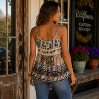 A woman stands in front of a boutique doorway wearing a bohemian-style patterned camisole top with thin straps and a tiered ruffle hem, paired with blue jeans.
