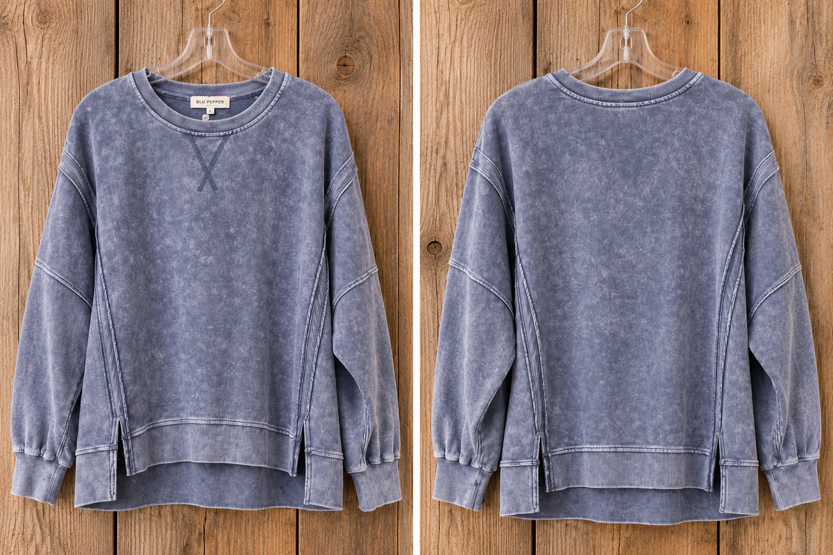 A slate blue acid-wash sweatshirt shown from both the front and back views, hanging on a clear hanger against a rustic wooden plank background.