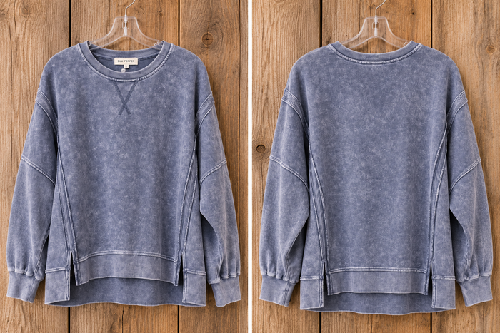 A slate blue acid-wash sweatshirt shown from both the front and back views, hanging on a clear hanger against a rustic wooden plank background.