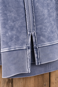 Close-up of a washed blue-gray garment with a vertical split seam and ribbed hem, photographed against a wooden surface.