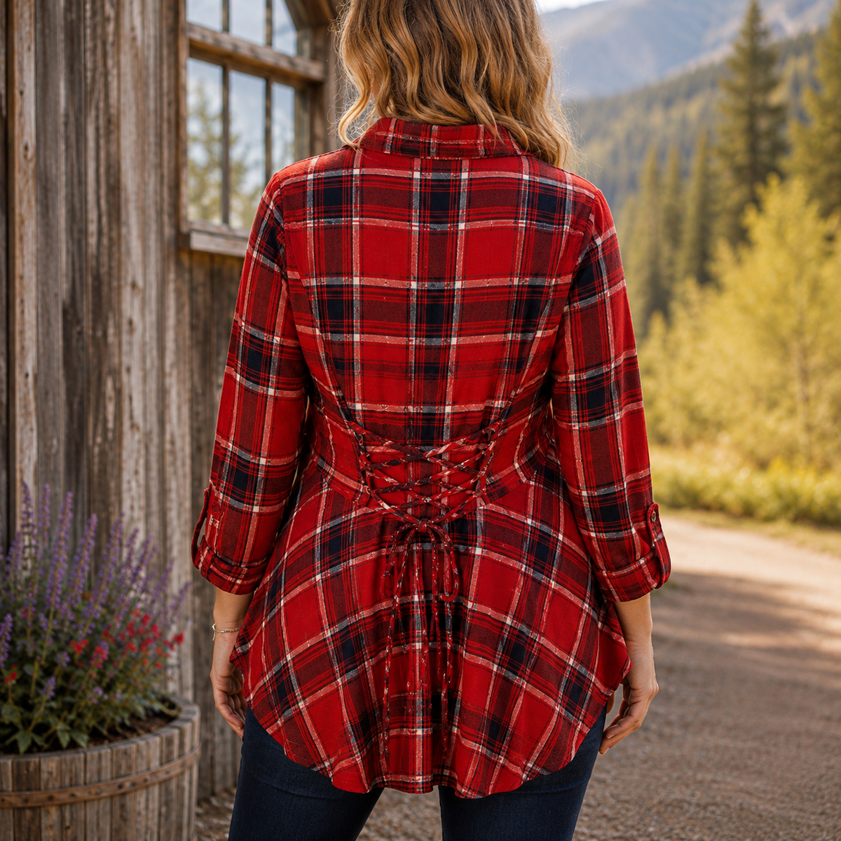 A woman viewed from behind wearing a red plaid button-up shirt with a lace-up tie waist, set against a rustic wooden cabin and mountain background.