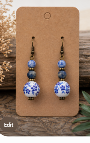 A pair of dangling earrings displayed on a brown card. Each earring has a dark metal fishhook, a small blue-and-white patterned bead, two medium blue beads, and a round white bead with blue floral motifs.