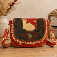 A red and navy beaded shoulder bag with gold and beige accents, displayed on a wooden surface with decorative dried plants and a vase in the background.