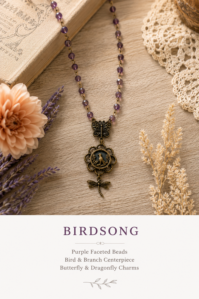 A necklace with purple faceted beads, a butterfly centerpiece, and dragonfly charms, styled on a wooden surface with dried flowers, lace, and a book. Text below reads 'BIRDSONG' and lists the product details.