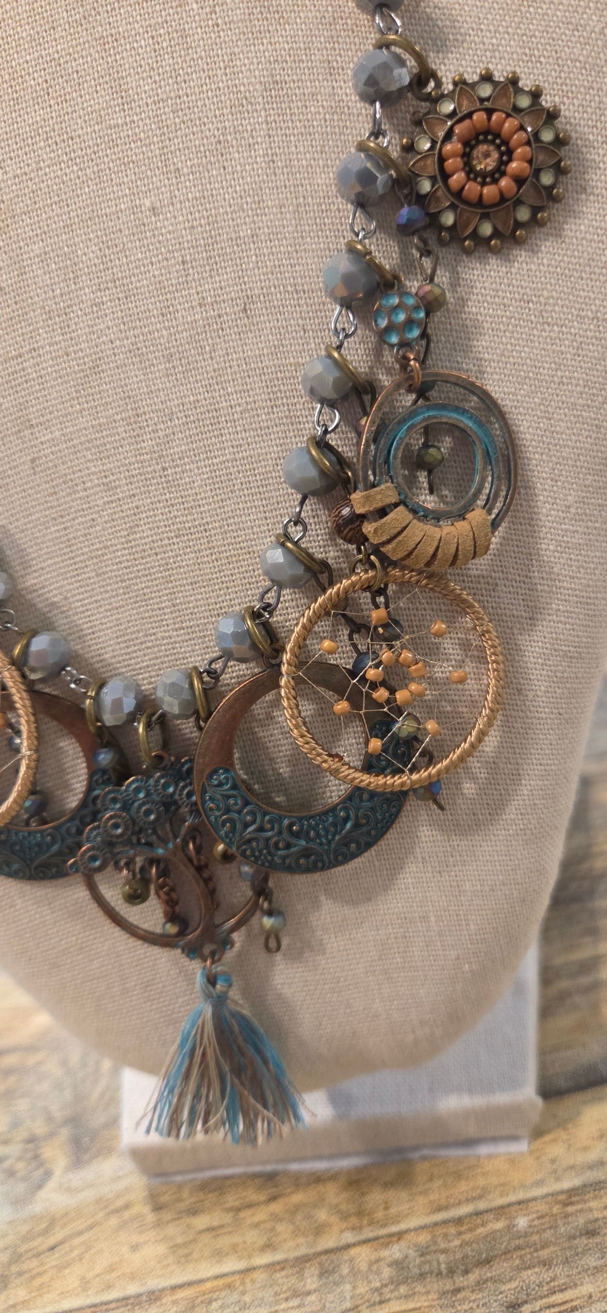 Close-up of boho necklace with turquoise tone charms, gray beads and woven circle details