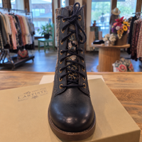 A dark navy leather lace-up ankle boot with gold eyelets and a leopard-print inner lining, displayed on top of a beige shoebox in a boutique setting.