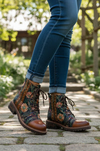 Person wearing floral-patterned boots and blue jeans on a stone path with greenery in the background