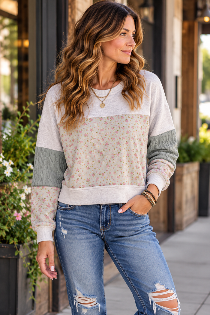 Woman standing outside on a sidewalk wearing the NewIn Sweater with floral print and textured cable knit panels.
