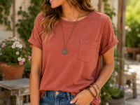 A woman wearing a rust-colored short-sleeve pocket t-shirt and blue jeans, standing in a garden patio setting.