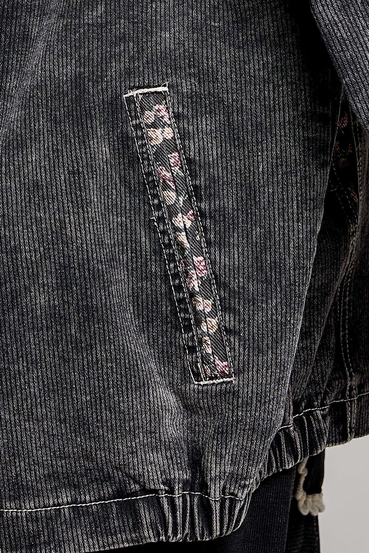 Close-up of a dark gray corduroy jacket featuring a vertical pocket with a pink and white floral patterned fabric trim.