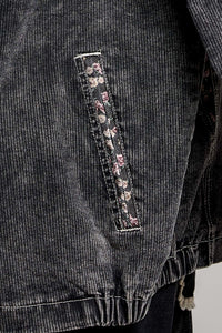 Close-up of a dark gray corduroy jacket featuring a vertical pocket with a pink and white floral patterned fabric trim.