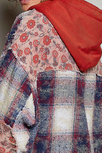 Close-up of a person wearing a patchwork hoodie with a red hood, a beige floral panel, and a distressed plaid patch in blue, red, and cream.