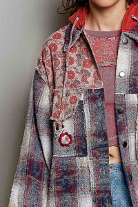 A close-up of a person wearing a layered fashion outfit featuring a heavily textured, patchwork-style plaid and floral jacket over a dusty rose ribbed top and blue jeans.