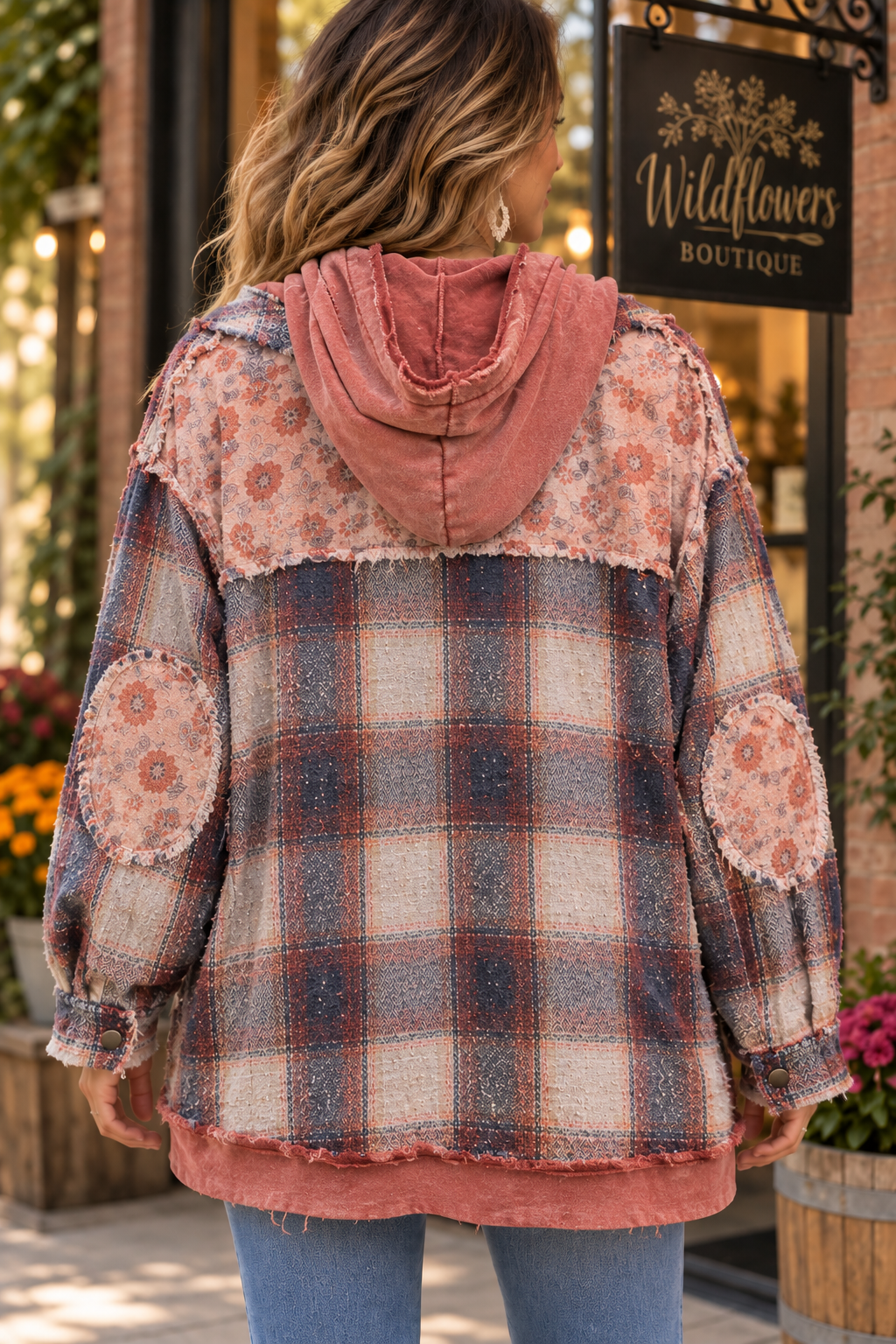 A woman viewed from behind wearing a patchwork hooded jacket with a distressed plaid pattern in muted blue, beige, and dusty rose, standing in front of a boutique storefront.