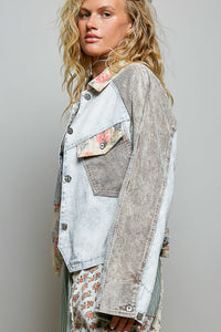 A woman wearing a mixed-media denim jacket with a light-wash front panel, brown corduroy sleeves, and floral patterned accents on the chest pocket and collar, photographed against a neutral gray background.