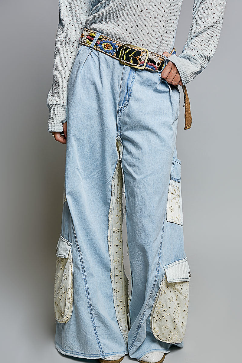 A person wearing light blue wide-leg denim cargo pants with cream patch pockets and a colorful patterned belt, paired with a white patterned long-sleeve top against a gray studio background.