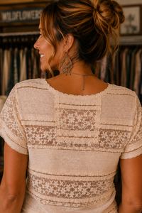 A woman shown from the back wearing a cream-colored short-sleeve blouse with intricate lace and floral embroidery patterns across the back and shoulders.