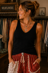 A woman wearing a black sleeveless lace top and red patterned bohemian pants with white lace trim, standing in a rustic clothing store.