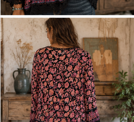 A woman shown from the back wearing a long-sleeve black blouse with a pink and coral floral pattern, standing in a rustic indoor setting with a wooden table, vase, and wall art in the background.