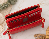 A red woven leather zip-around wallet shown open on a light marble surface with decorative fabric and wood props around it.